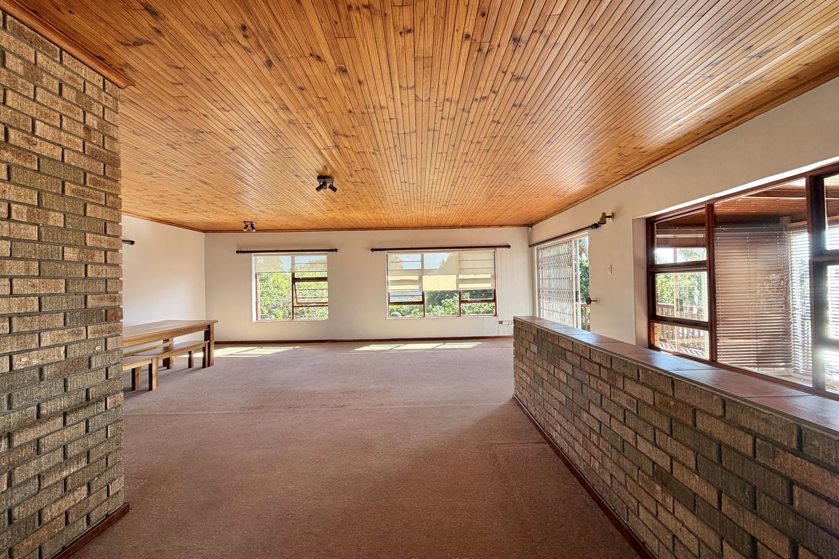 Spacious living area featuring a warm timber tongue and groove ceiling, exposed brick accents, and large windows providing ample natural light.