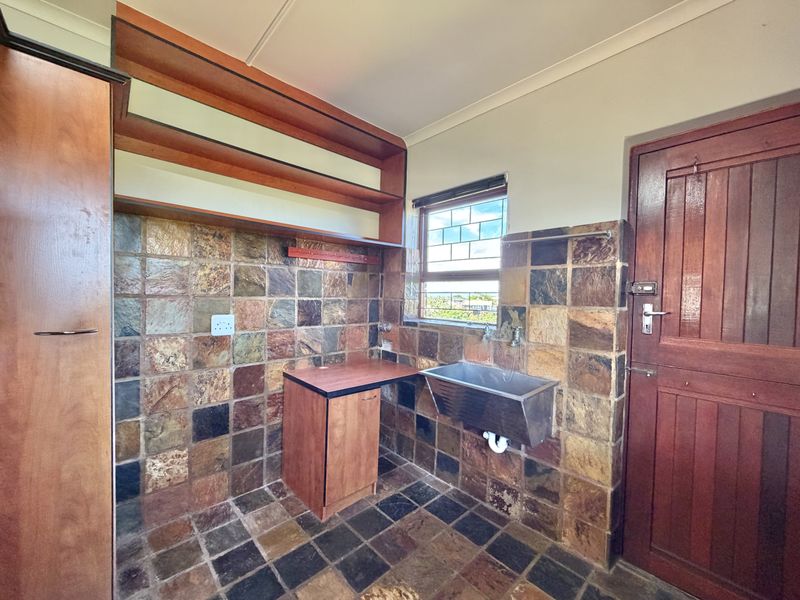 A functional laundry area featuring stone wall and floor tiles, a stainless steel utility sink, built-in wooden cabinetry, and open shelving.