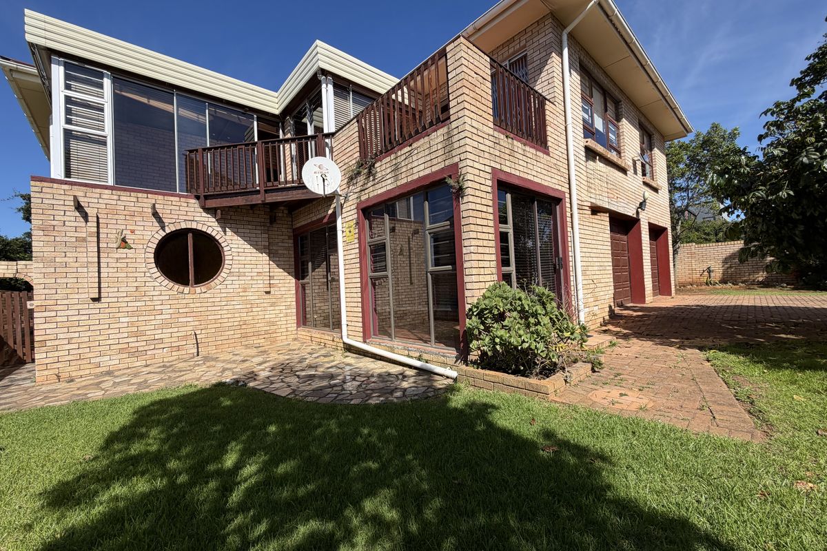 Rear view of a multi-story brick house featuring a balcony, paved patio area, and integrated garage access.