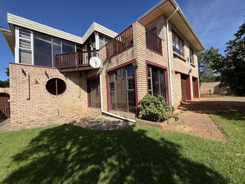 Rear view of a multi-story brick house featuring a balcony, paved patio area, and integrated garage access.