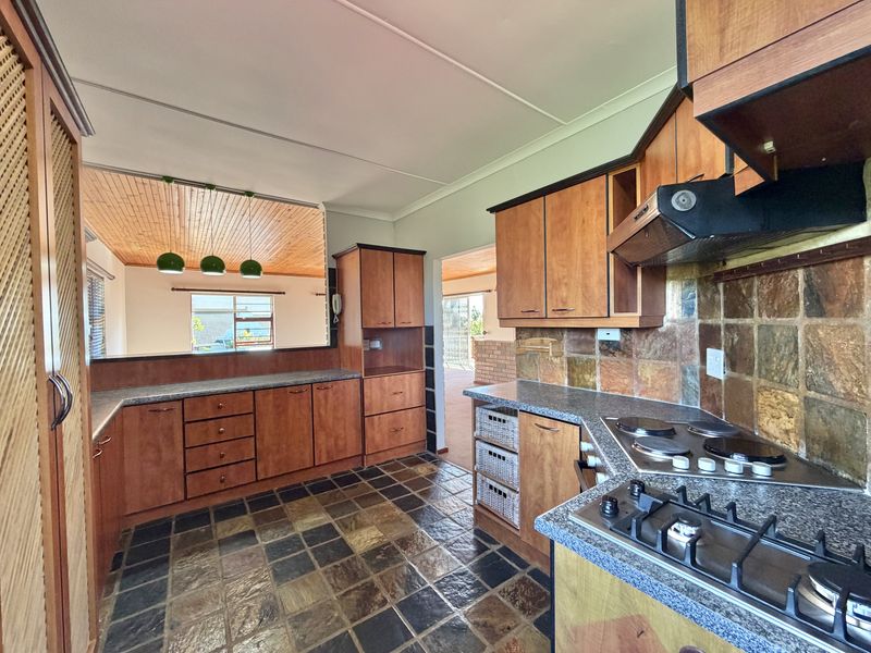 A functional kitchen featuring wooden cabinetry, granite countertops, dual hobs, and a convenient pass-through window overlooking the adjacent living area.