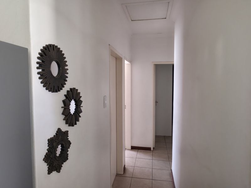 A clean, neutral hallway featuring tiled flooring and a ceiling access hatch, providing access to multiple rooms within the home.