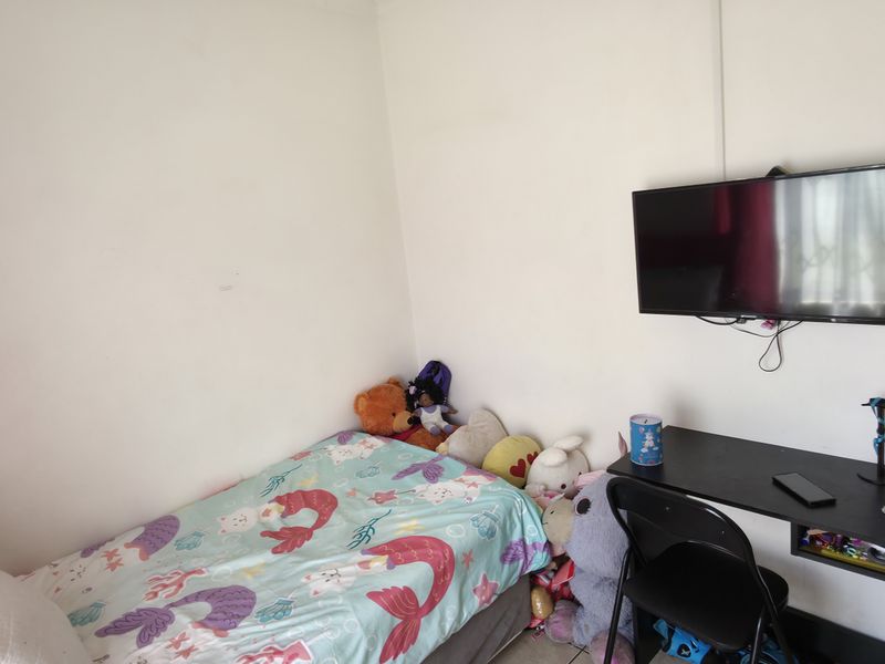 A compact bedroom featuring a wall-mounted television and neutral wall finishes, offering a functional space for rest or study.