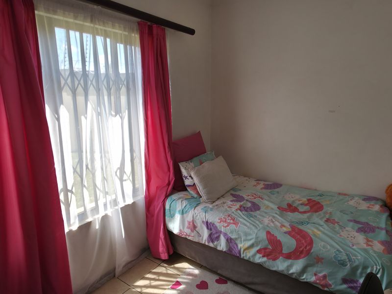 A compact bedroom featuring tiled flooring and a window fitted with a security gate, providing natural light.