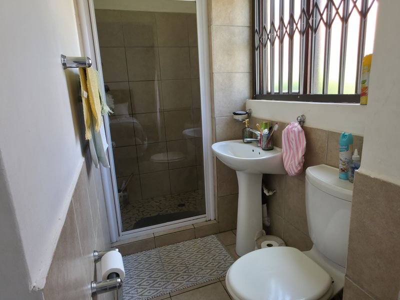 A functional bathroom featuring a pedestal sink, toilet, and a separate shower enclosure with tiled finishes and a security-gated window.