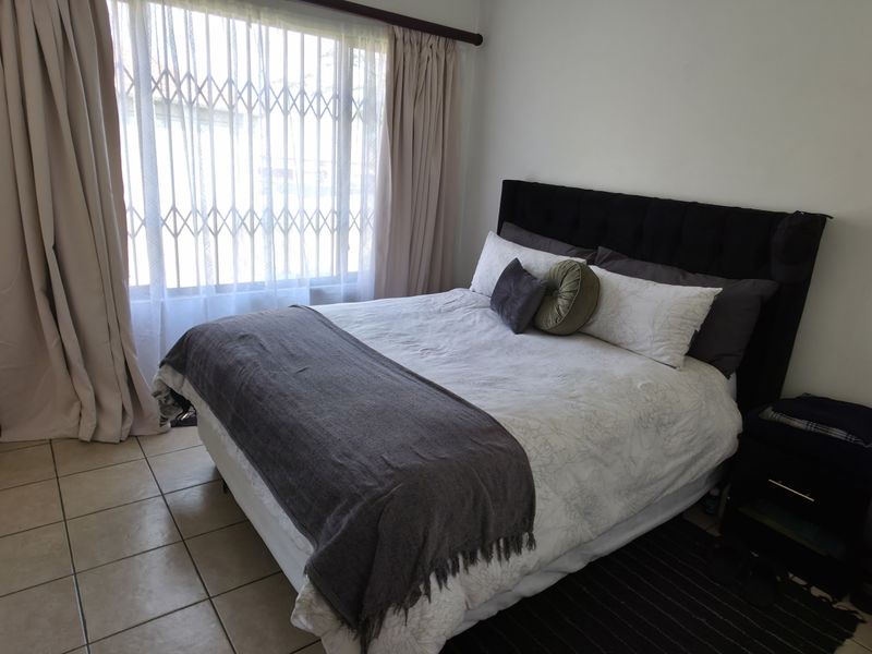 A functional bedroom featuring tiled flooring and a window fitted with a security gate and curtains.