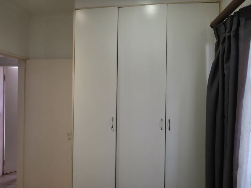A bedroom featuring built-in cupboards and a window with a security gate, offering a clean and functional space.