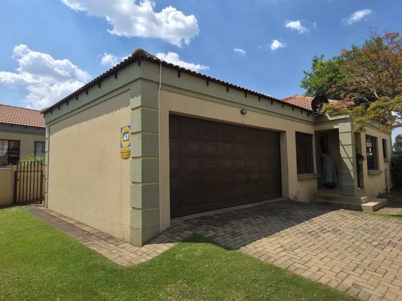 Front exterior view of the property featuring a paved driveway, single garage, and well-maintained garden area with boundary walling.