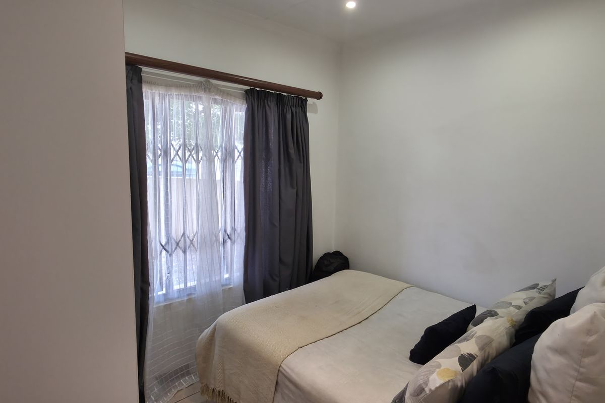 A compact bedroom featuring neutral walls, recessed lighting, and a window fitted with a security gate and curtain rod.