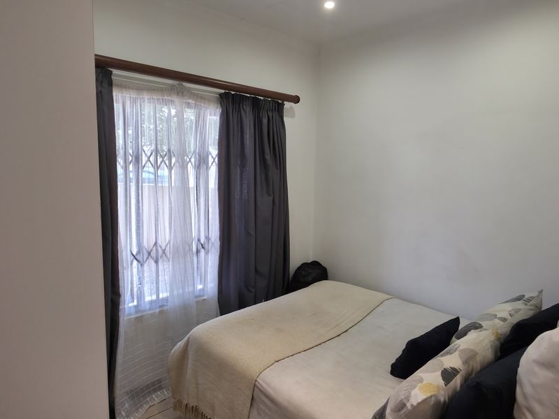 A compact bedroom featuring neutral walls, recessed lighting, and a window fitted with a security gate and curtain rod.