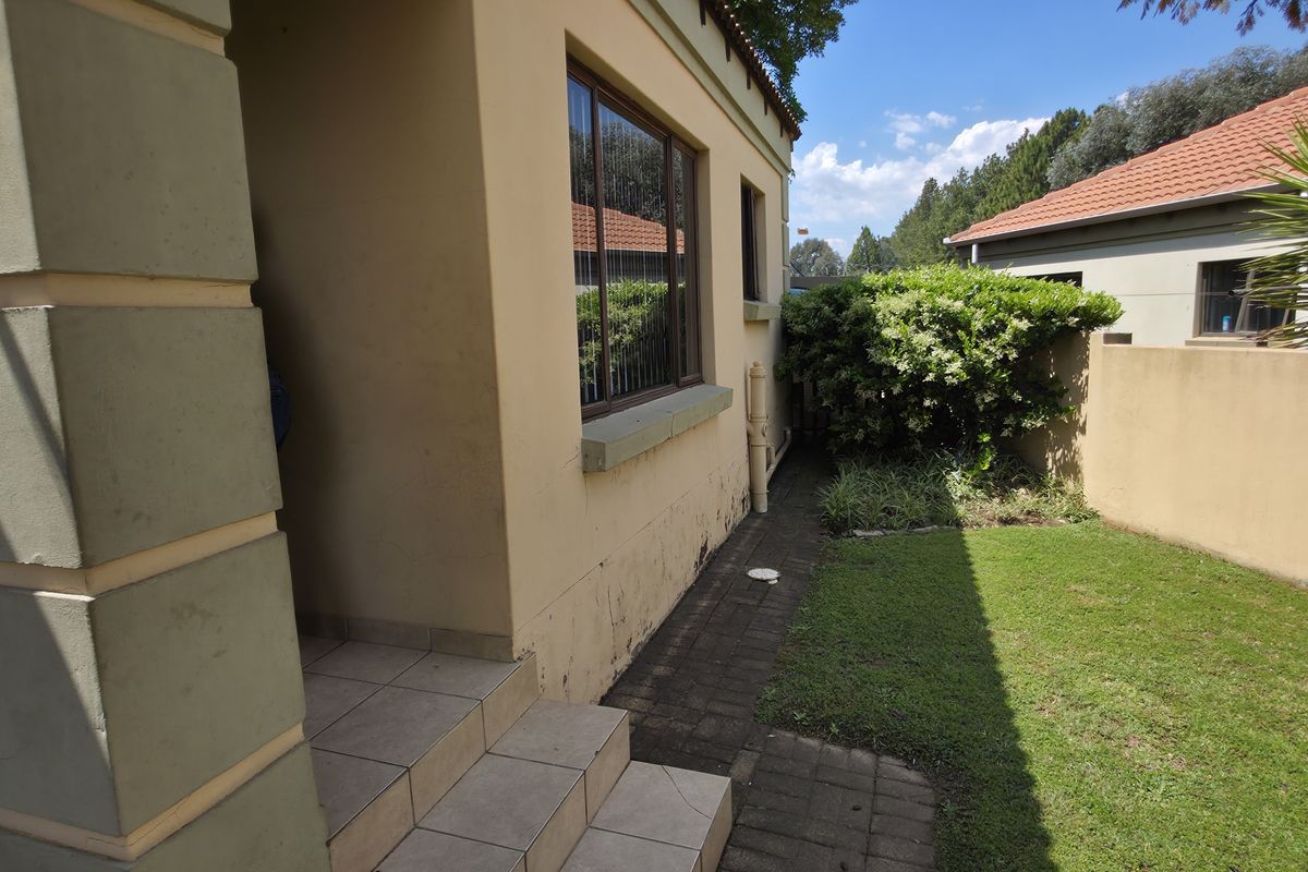 A view of the rear exterior area featuring a small lawn, paved walkway, and tiled steps leading to the building entrance.