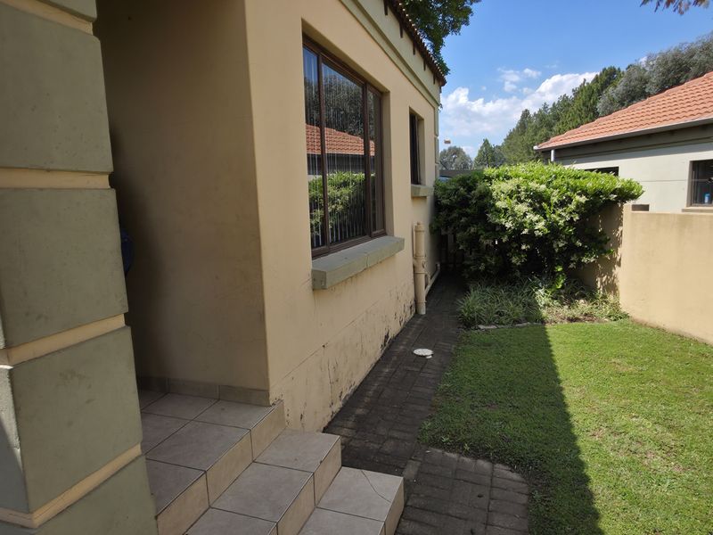A view of the rear exterior area featuring a small lawn, paved walkway, and tiled steps leading to the building entrance.