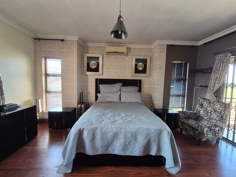 A well-maintained bedroom featuring laminate flooring, split-system air conditioning, and dual windows with venetian blinds, offering a comfortable and functional living space.