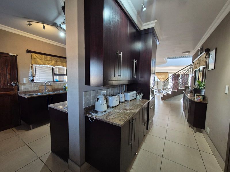 A spacious kitchen featuring dark wood cabinetry, granite countertops, and tiled flooring, with an open-plan layout leading towards the staircase.