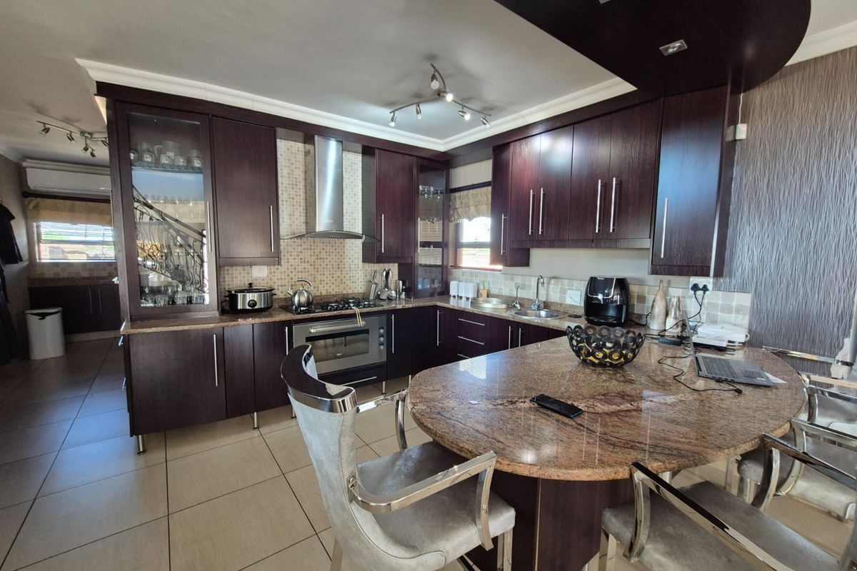 A well-appointed kitchen featuring dark wood cabinetry, granite countertops, a central breakfast island, and integrated stainless steel appliances with tiled flooring.