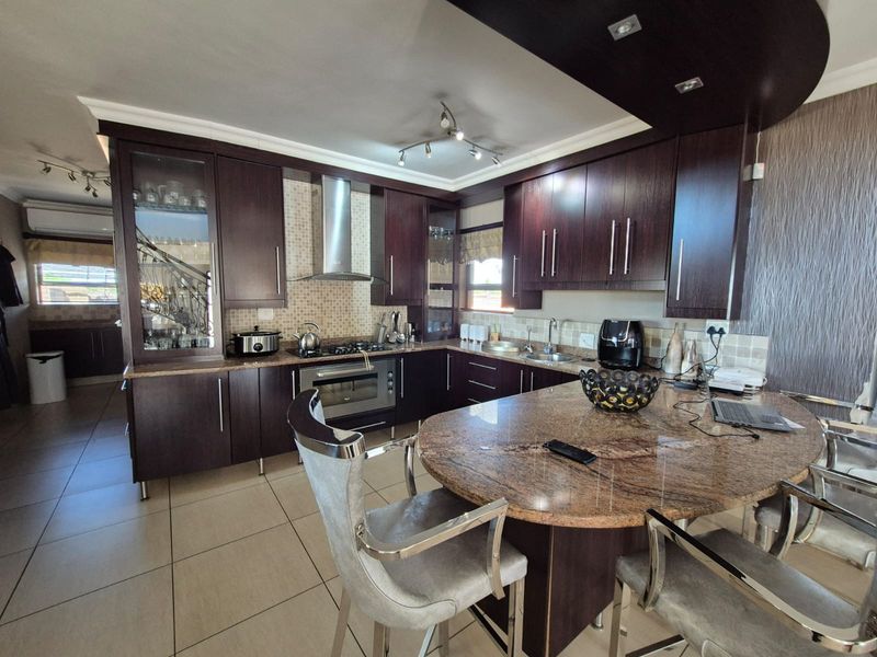 A well-appointed kitchen featuring dark wood cabinetry, granite countertops, a central breakfast island, and integrated stainless steel appliances with tiled flooring.
