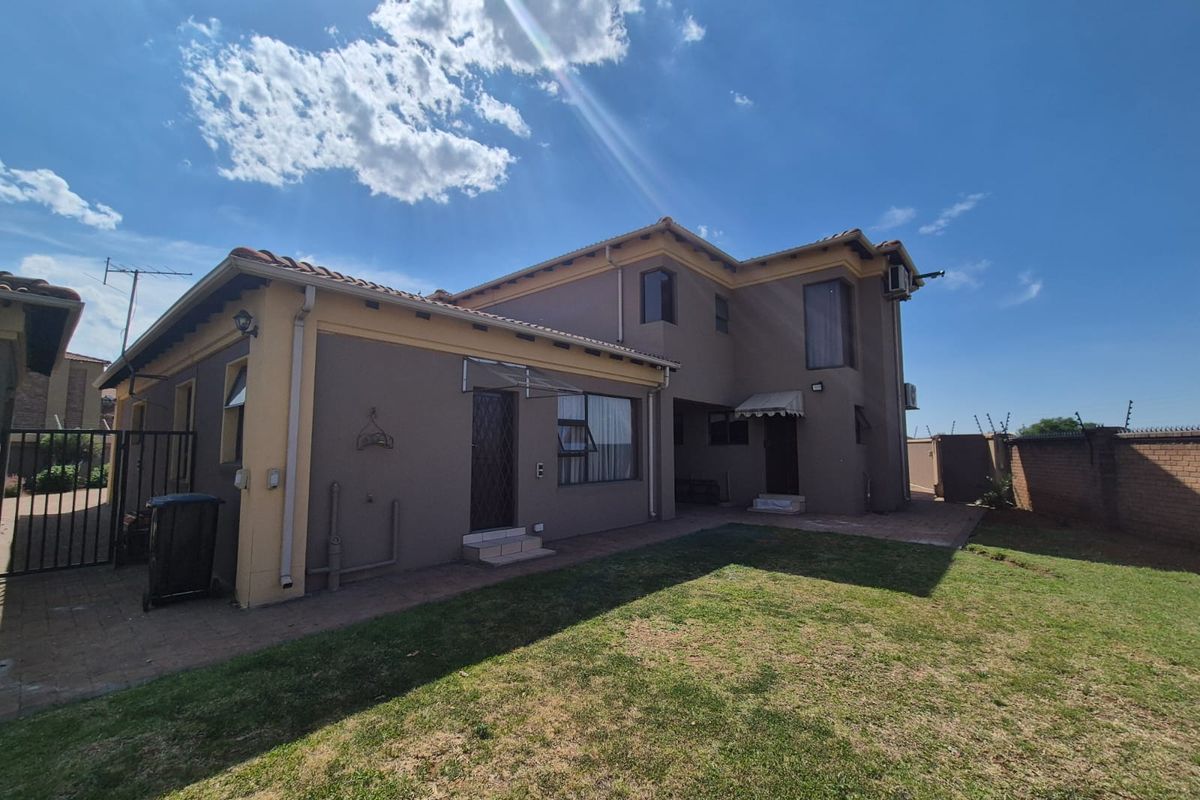 Rear view of the house featuring a paved patio area, lawn, and perimeter walling with security features.