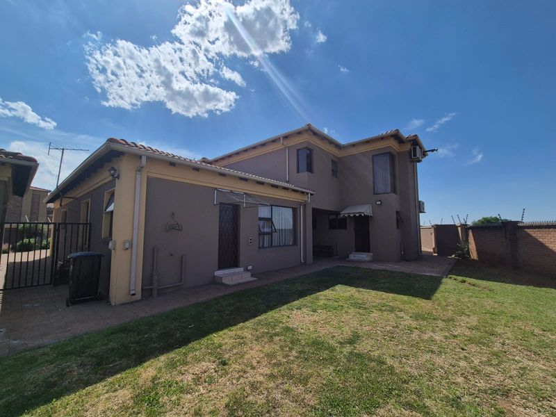Rear view of the house featuring a paved patio area, lawn, and perimeter walling with security features.