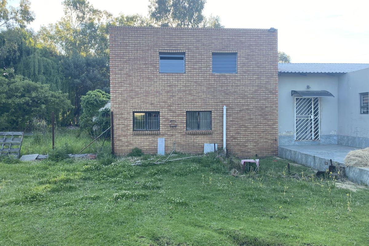 Rear view of a face brick building featuring a small concrete patio, security gates, and metal window bars, set against a large grassy yard.