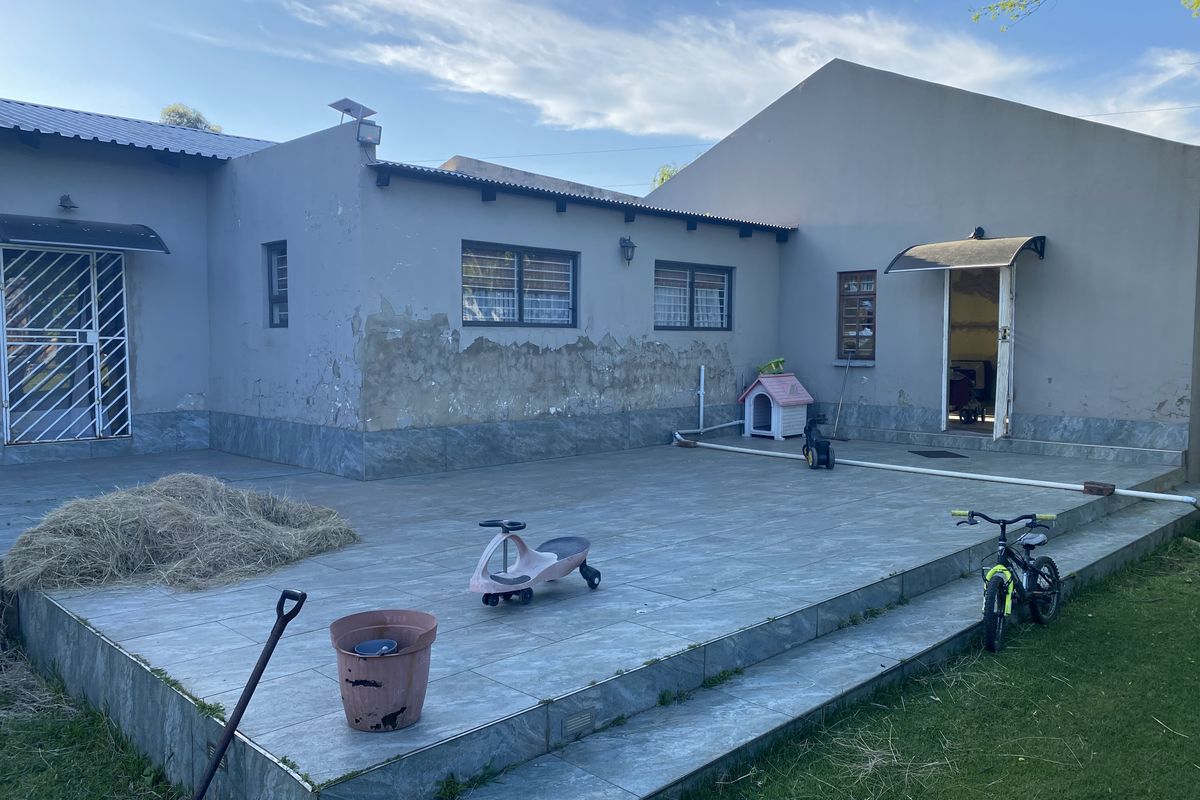Rear exterior view of the property featuring a tiled patio area, security gates, and external wall finishes requiring maintenance and repair.