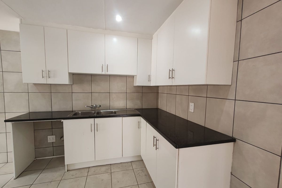 A clean, functional kitchen featuring white cabinetry, black granite countertops, and a stainless steel double sink with neutral tiled backsplash and flooring.