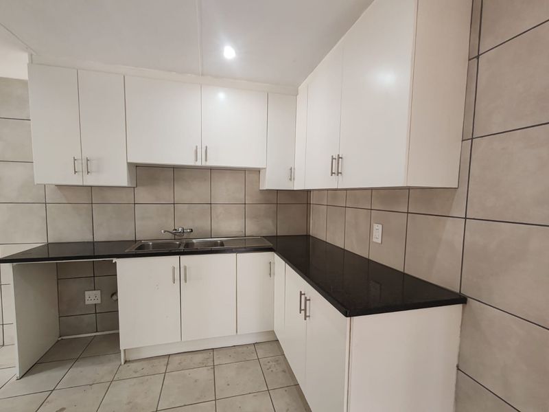 A clean, functional kitchen featuring white cabinetry, black granite countertops, and a stainless steel double sink with neutral tiled backsplash and flooring.