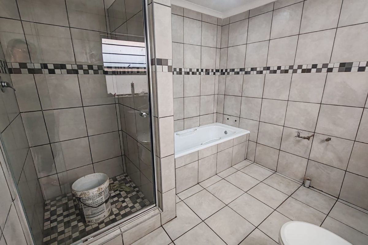 A spacious bathroom featuring a glass shower enclosure and a built-in bathtub, currently requiring completion of plumbing fixtures and final finishes.