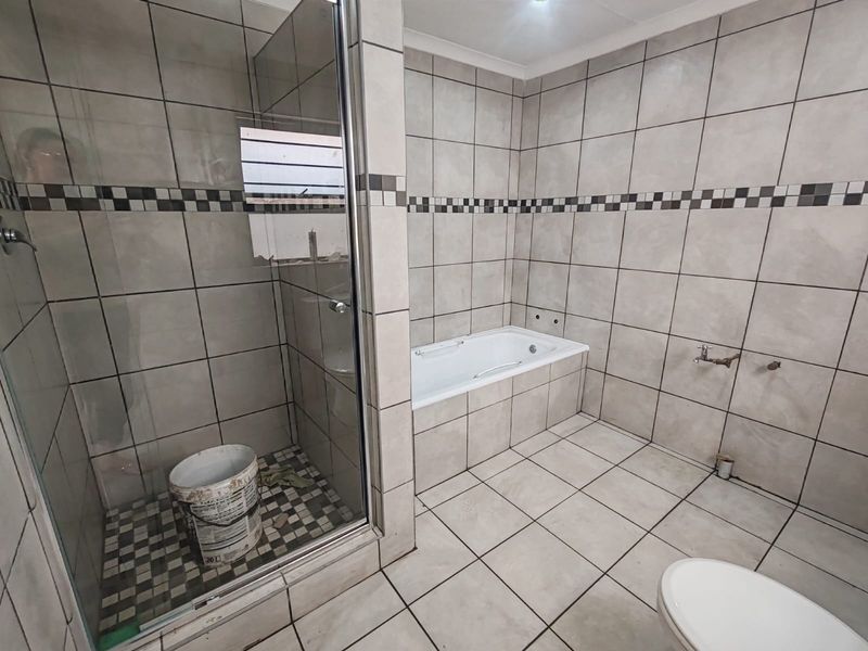 A spacious bathroom featuring a glass shower enclosure and a built-in bathtub, currently requiring completion of plumbing fixtures and final finishes.