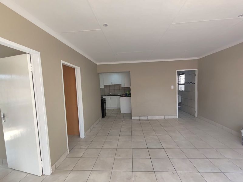 An open-plan living area featuring neutral wall tones, tiled flooring, and a view into the adjacent kitchen and bathroom spaces.