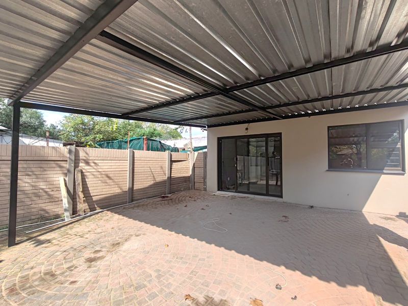 A covered outdoor patio area featuring paved flooring, a corrugated metal roof structure, and direct access to the interior through sliding glass doors.