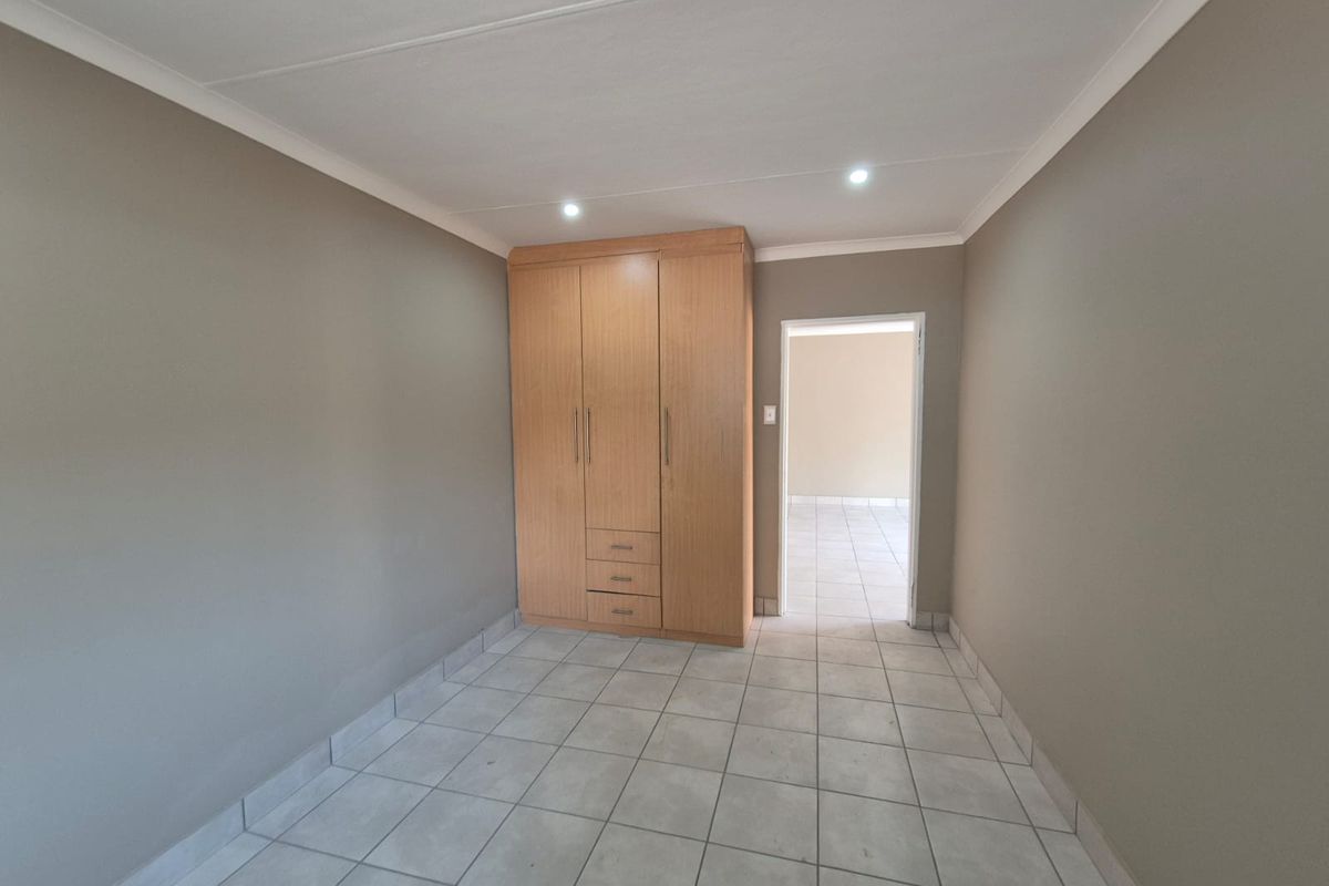 A clean, empty bedroom featuring neutral wall tones, tiled flooring, and a functional built-in wooden wardrobe.