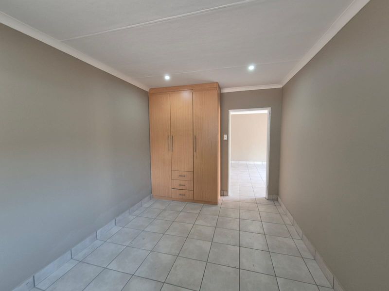 A clean, empty bedroom featuring neutral wall tones, tiled flooring, and a functional built-in wooden wardrobe.