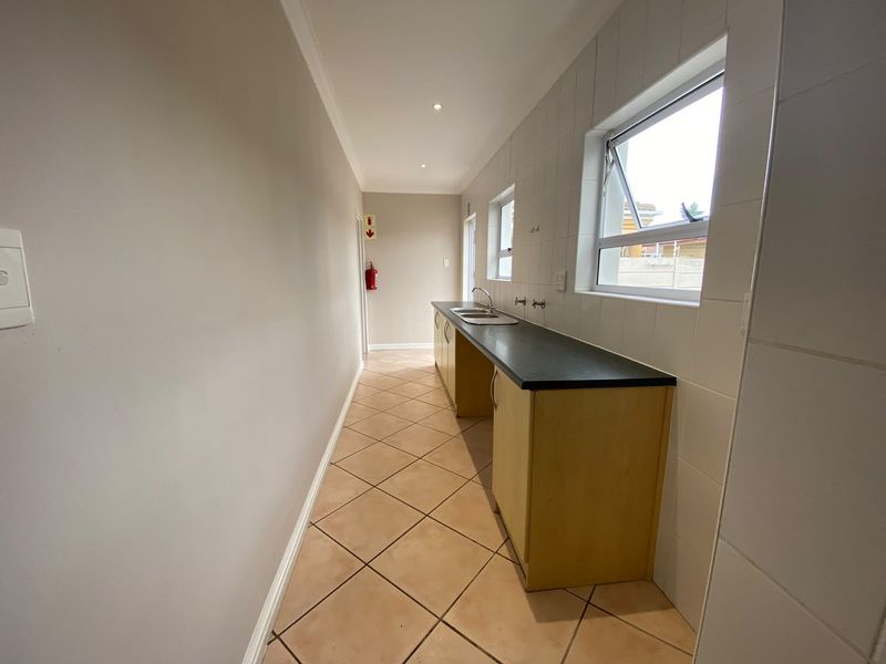 A functional scullery or laundry area featuring built-in cabinetry, a laminate countertop with a stainless steel sink, and tiled finishes throughout.