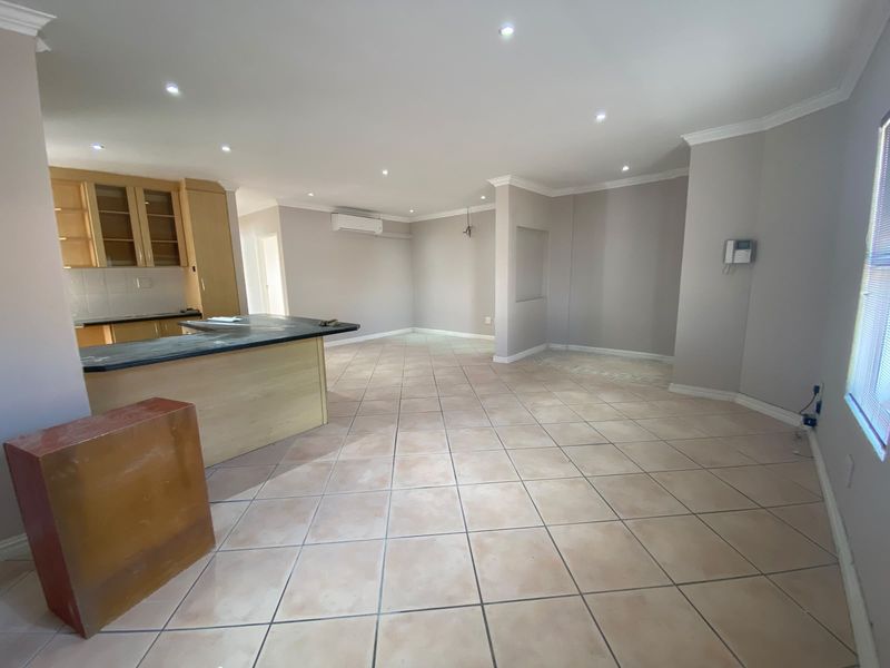 Spacious open-plan living and kitchen area featuring neutral walls, ceramic tiled flooring, recessed lighting, and built-in cabinetry with stone countertops.