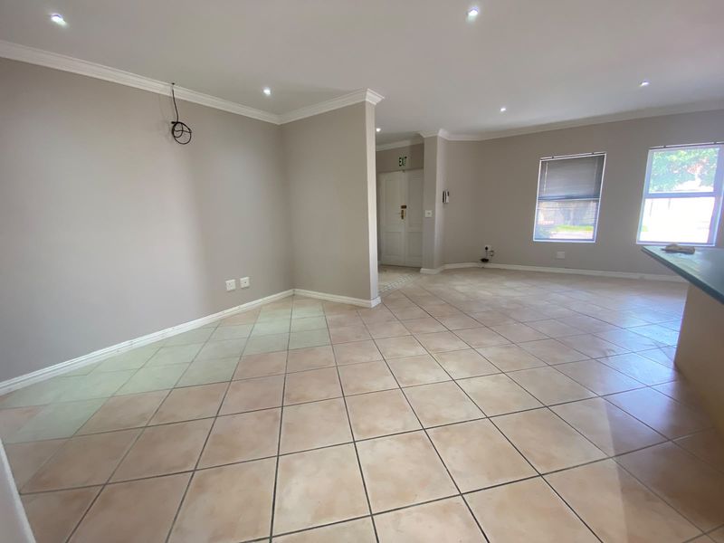 Spacious open-plan living area featuring neutral wall tones, ceramic tiled flooring, recessed downlighting, and a double-door entrance.