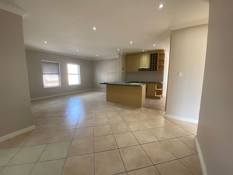 Spacious open-plan living area featuring tiled flooring, recessed downlights, and a functional kitchen with built-in cabinetry and a central island.