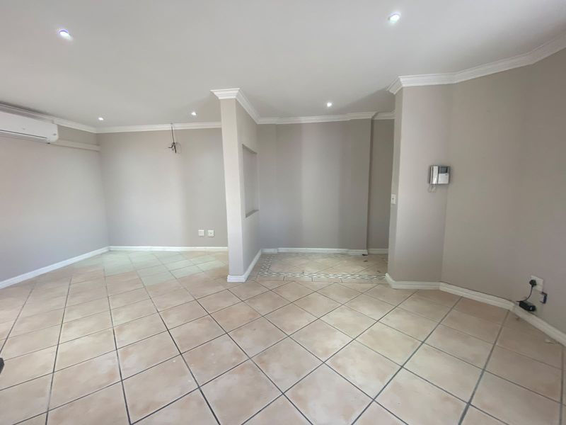An empty, open-plan living area featuring neutral tiled floors, recessed lighting, coving, and an installed air conditioning unit.