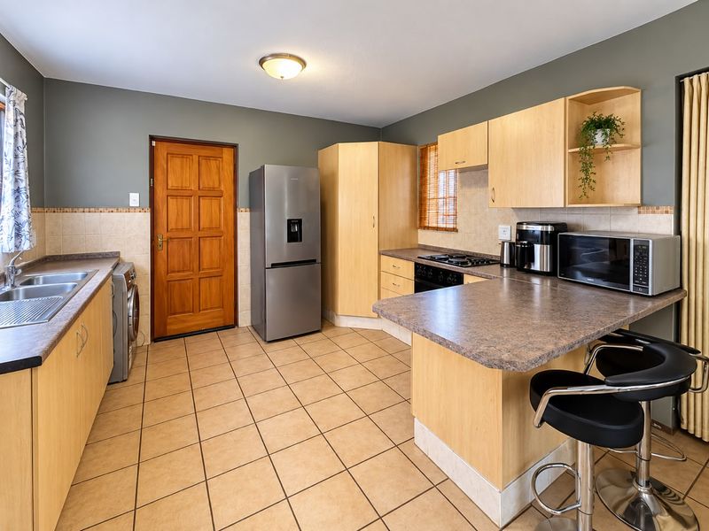 Functional kitchen featuring light wood cabinetry, laminate countertops, a gas hob, built-in oven, and tiled flooring with a breakfast bar area.