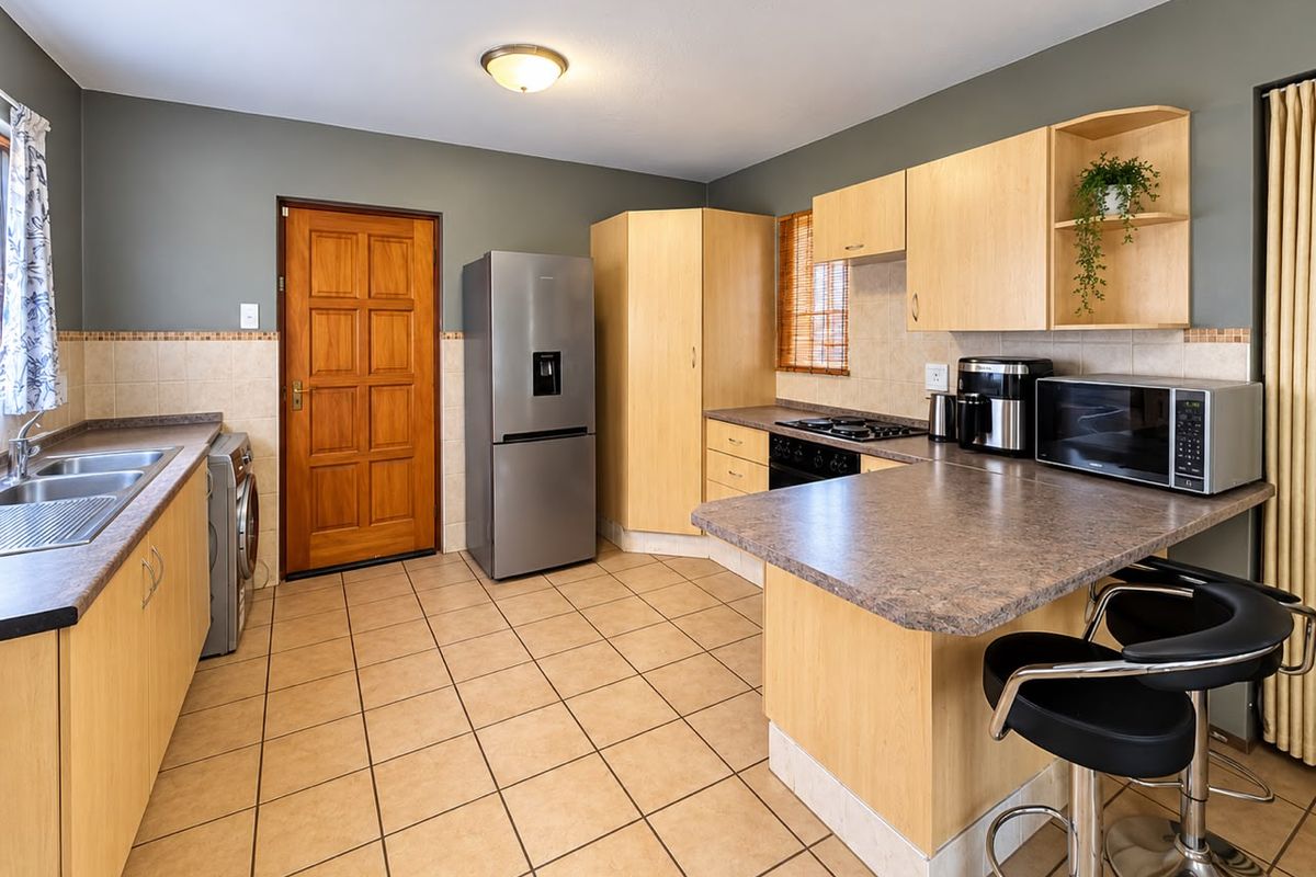 Functional kitchen featuring light wood cabinetry, laminate countertops, a gas hob, built-in oven, and tiled flooring with a breakfast bar area.