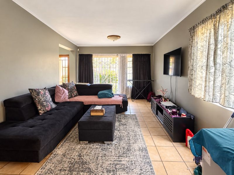 A spacious living room featuring tiled flooring, neutral wall tones, and a security gate leading to the exterior.