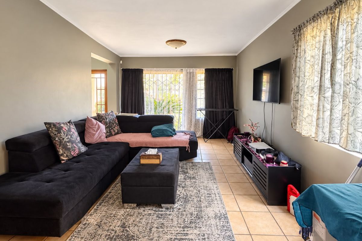 A spacious living room featuring tiled flooring, neutral wall tones, and a security gate leading to the exterior.