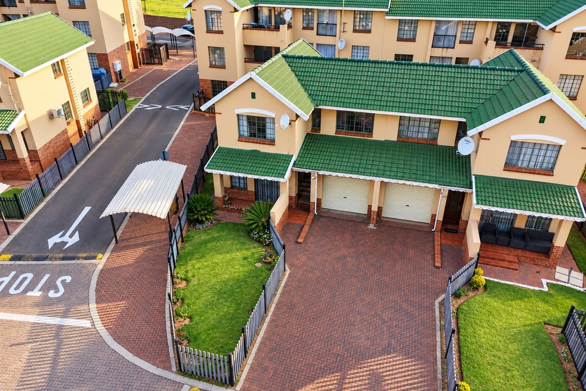 Aerial view of a townhouse complex featuring paved driveways, double garages, green tiled roofs, and well-maintained garden areas.