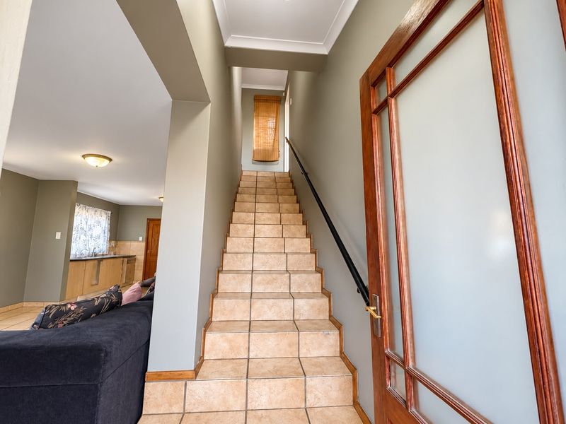 A bright hallway featuring a tiled staircase with a metal handrail, leading to an upper level, adjacent to an open-plan living and kitchen area.