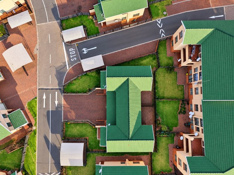 Aerial view of a townhouse complex featuring green metal roofs, paved driveways, private gardens, and designated carport parking areas.