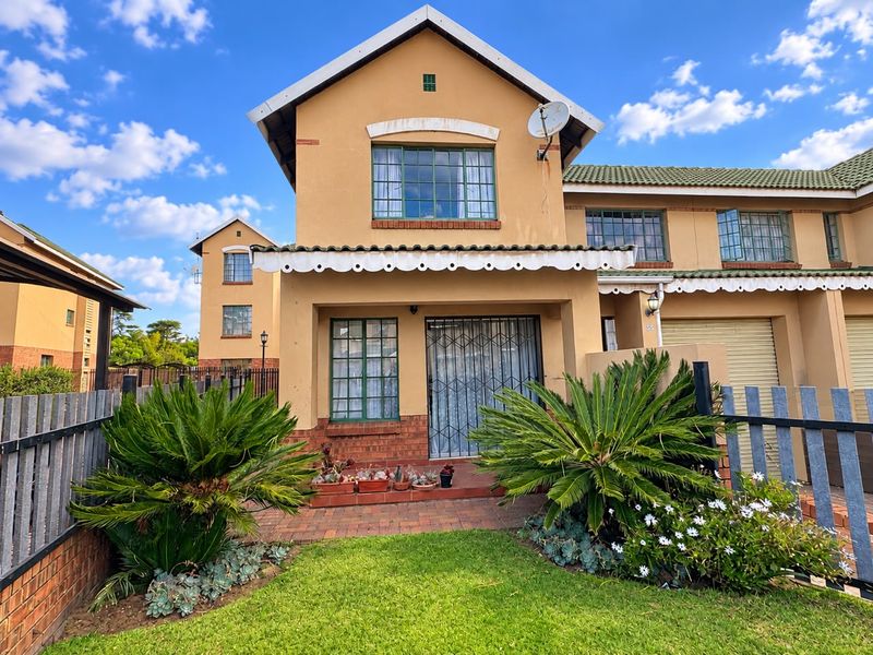 Front elevation of a townhouse featuring a tiled roof, brick facade, security gate, and a small landscaped garden with a paved entrance path.