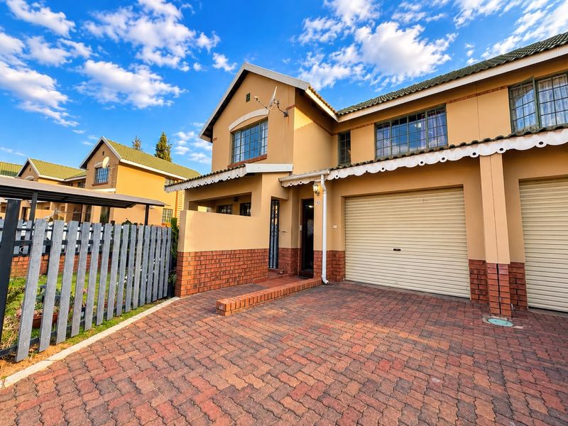 Front elevation of a townhouse featuring a brick paved driveway, roll-up garage door, and a tiled roof with a classic architectural design.