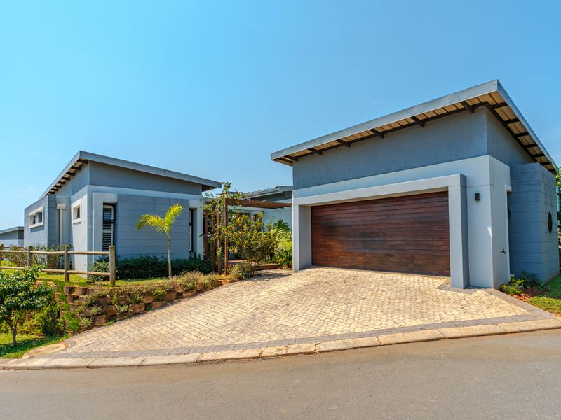 Modern townhouse exterior featuring a paved driveway, timber garage door, and a timber pergola, set within a well-maintained landscaped environment.