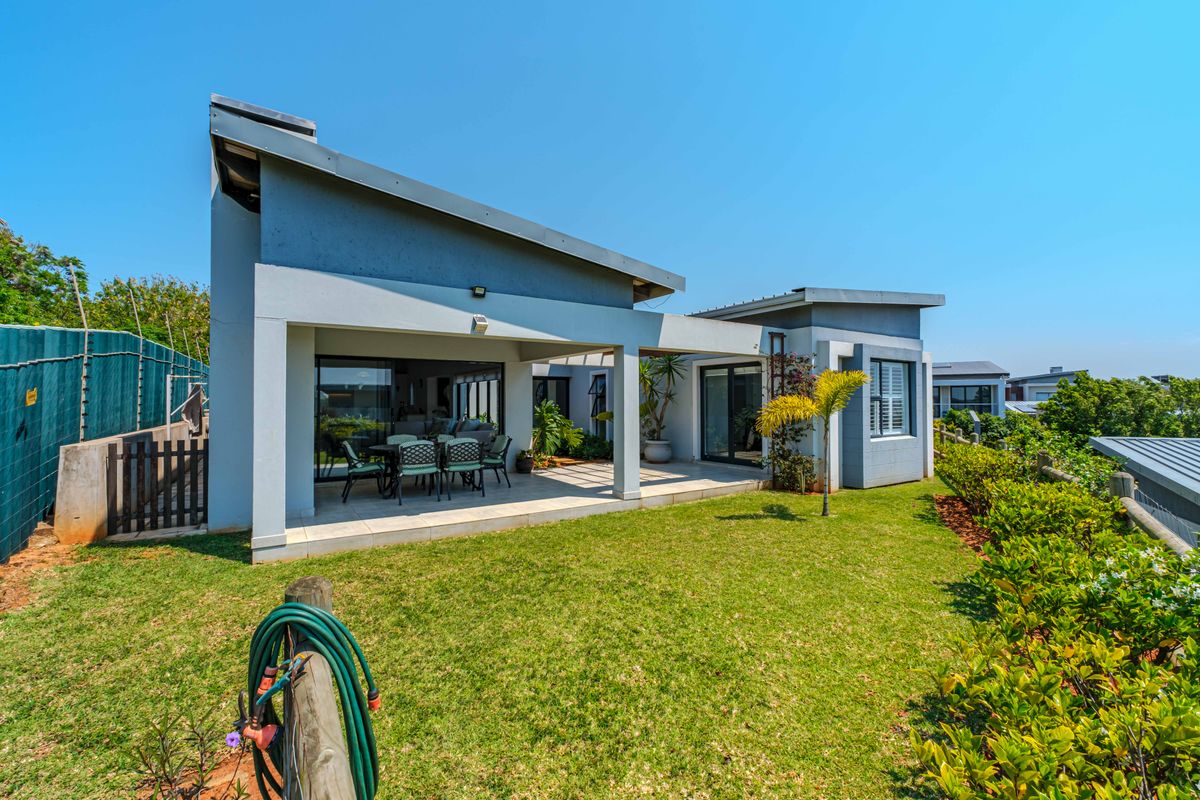 Rear view of the townhouse featuring a spacious covered patio with tiled flooring, sliding glass doors, and a well-maintained private garden.