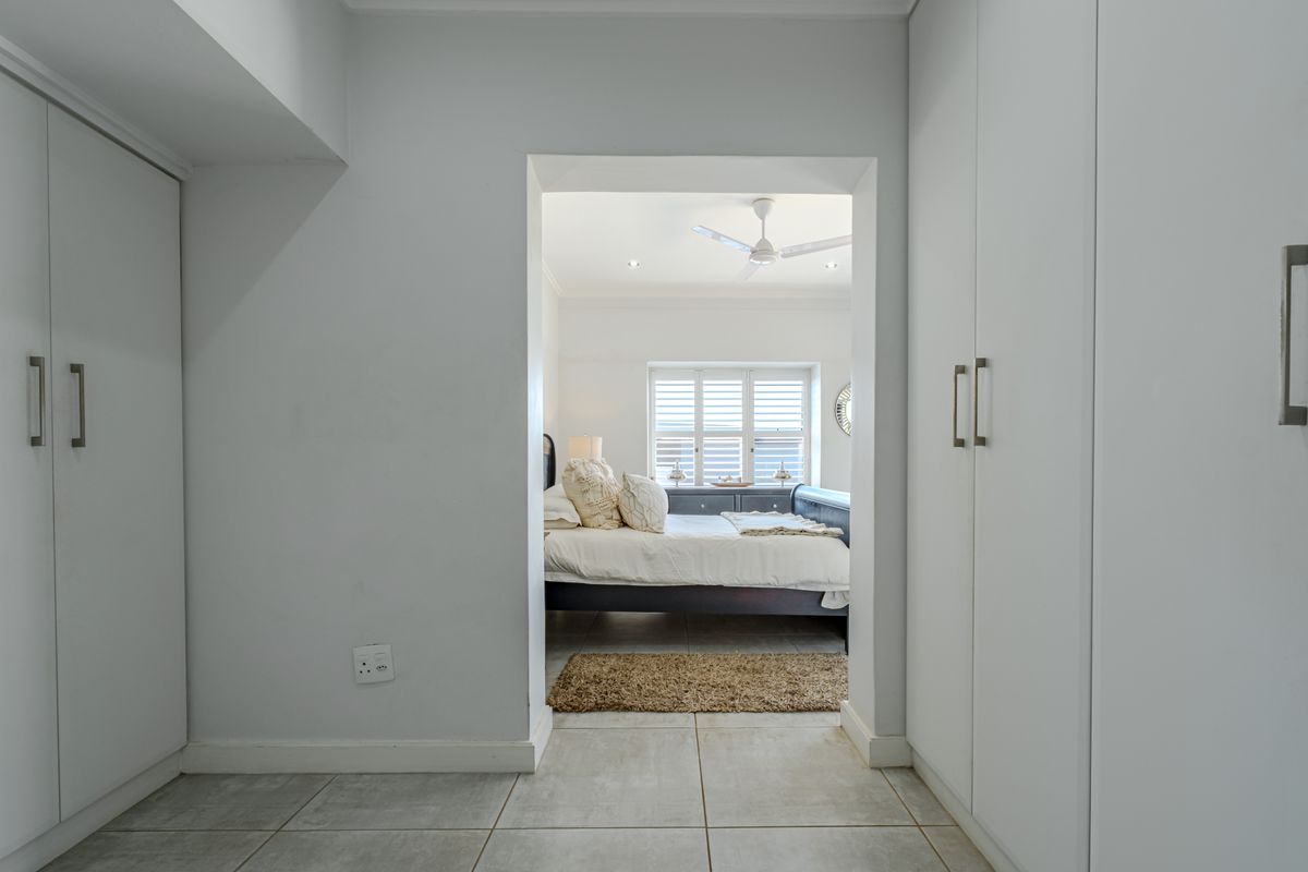 A well-maintained bedroom featuring built-in cupboards, tiled flooring, and a ceiling fan, with plantation shutters providing natural light control.