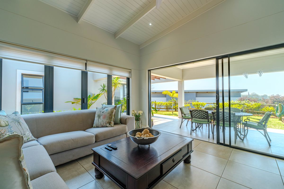 Bright and airy living room featuring vaulted ceilings, tiled floors, and large sliding glass doors that open onto a covered patio area.